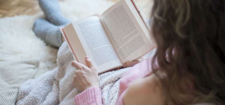 Coziness at home with the Hygge lifestyle. Photo of girl doing reading a book covered with a warm blanket.