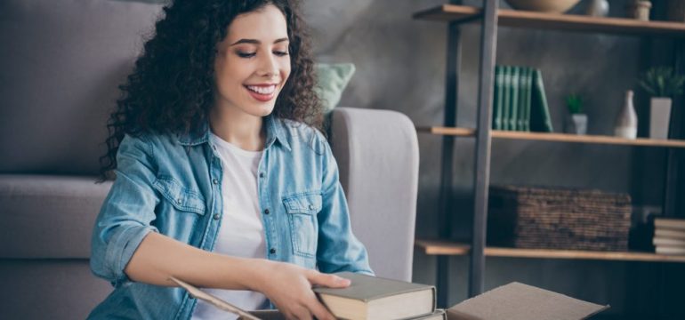 Attractive, cheerful wavy-haired female unpacking books as she moves into a modern loft. Shows trend of single women buying their own homes.