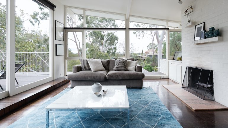 Mid-century modern home with living room with huge windows and large fireplace.