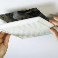 Close up horizontal photo of female hands removing bathroom exhaust fan cover from ceiling to clean it.