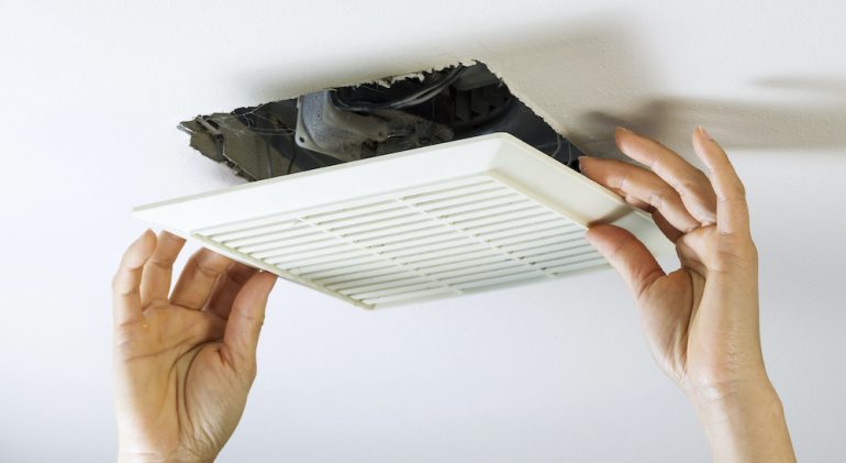 Close up horizontal photo of female hands removing bathroom exhaust fan cover from ceiling to clean it.