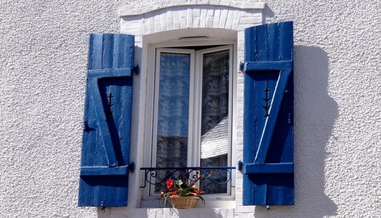 Window with blue shutters and window box with red flowers.