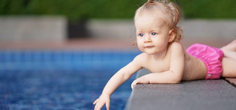 Little baby girl near swimming pool outdoors at risk of drowning accident.