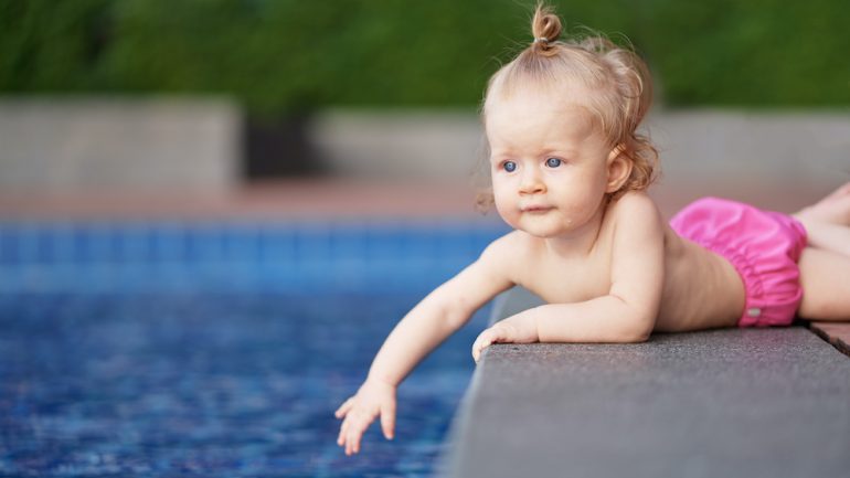 Little baby girl near swimming pool outdoors at risk of drowning accident.