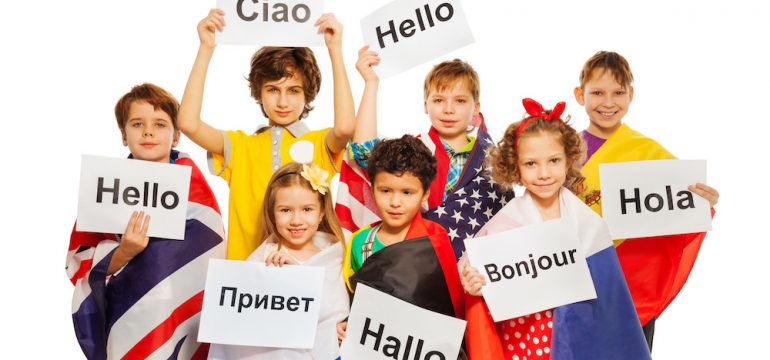 Expat children wrapped in flags of USA and European nations, holding greeting signs in different foreign languages.