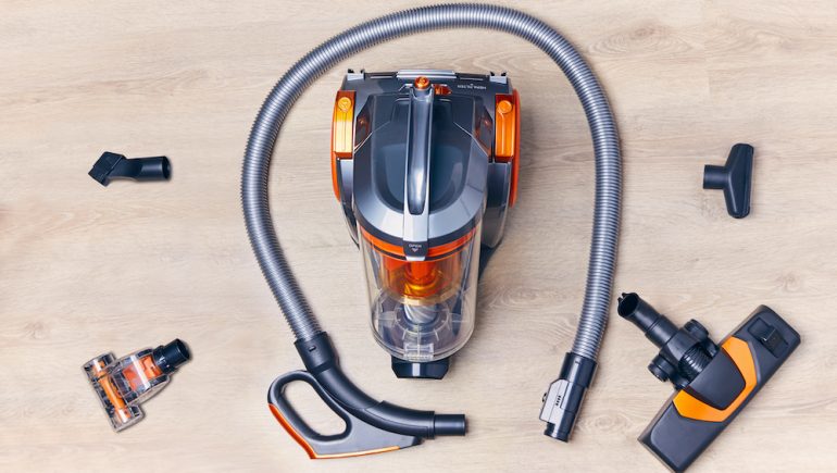 Top view of a modern vacuum cleaner with attachments for the hose spread out around the canister.