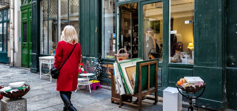 Consignment furniture and accessories shop on a side street in an historic neighborhood. Items for sale on the sidewalk. An unidentified woman in a red coat walks by.