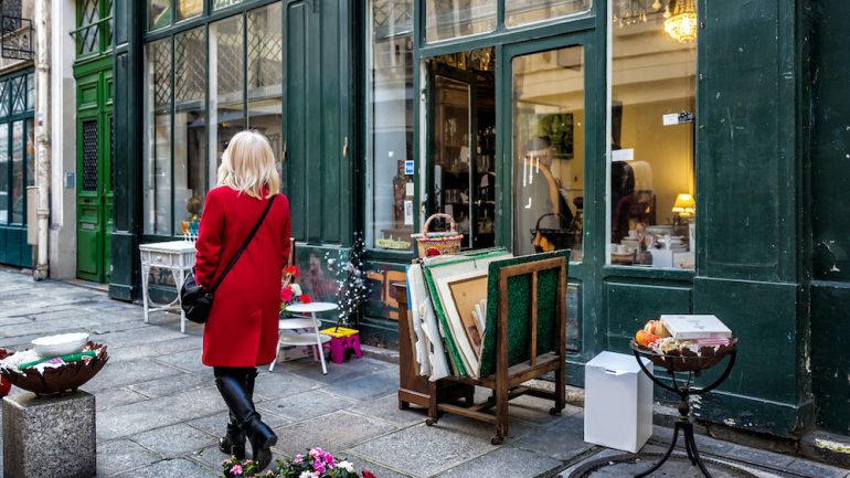 Consignment furniture and accessories shop on a side street in an historic neighborhood. Items for sale on the sidewalk. An unidentified woman in a red coat walks by.