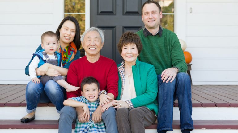 Multigenerational Chinese and Caucasian family portrait sitting on the front stairs of a home.