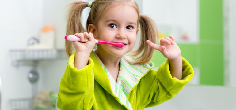 Smiling young girl brushing her teeth in a kids' bathroom.