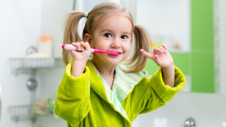 Smiling young girl brushing her teeth in a kids' bathroom.