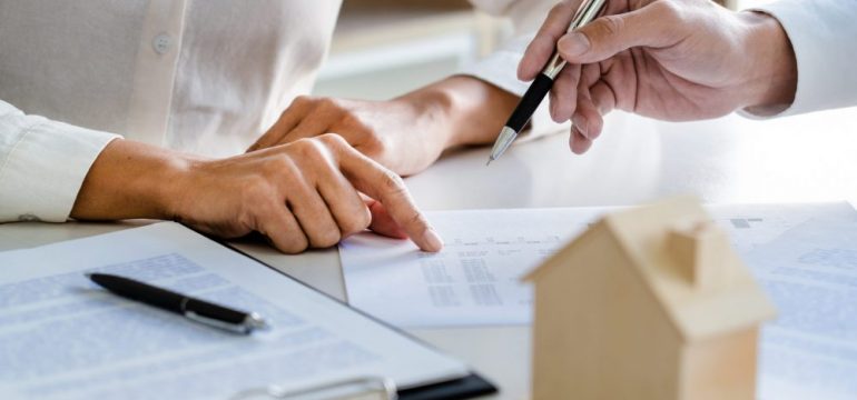 Real estate agent reviewing a mortgage loan contingency with a home buyer customer. Showing discussion over contract on a table with a wooden model home.