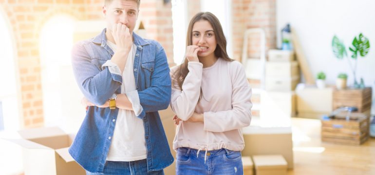 BeYoung couple moving to a new house looking stressed and nervous with hands on mouth biting nails. They are nervous about giving early possession to the home buyers.