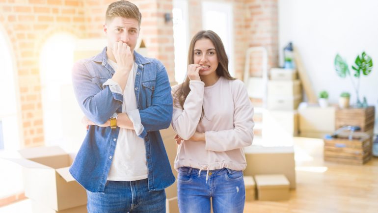 BeYoung couple moving to a new house looking stressed and nervous with hands on mouth biting nails. They are nervous about giving early possession to the home buyers.