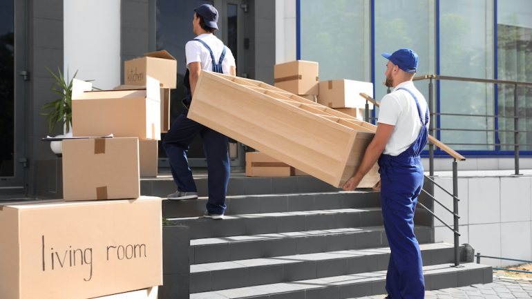 Male movers carrying shelving unit into new house. Concept of avoiding rogue moving companies.