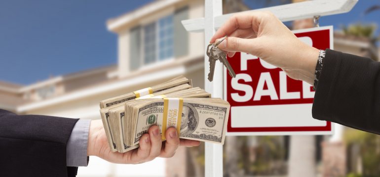 Real estate agent handing over the keys as home buyer is handing over all-Cash for home purchase. House with "For Sale Sign" in background.