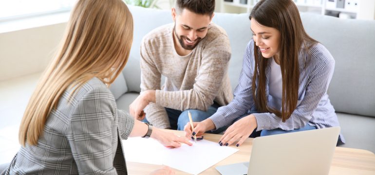 Young couple in office of real estate agent signing a listing agreement to sell their home.