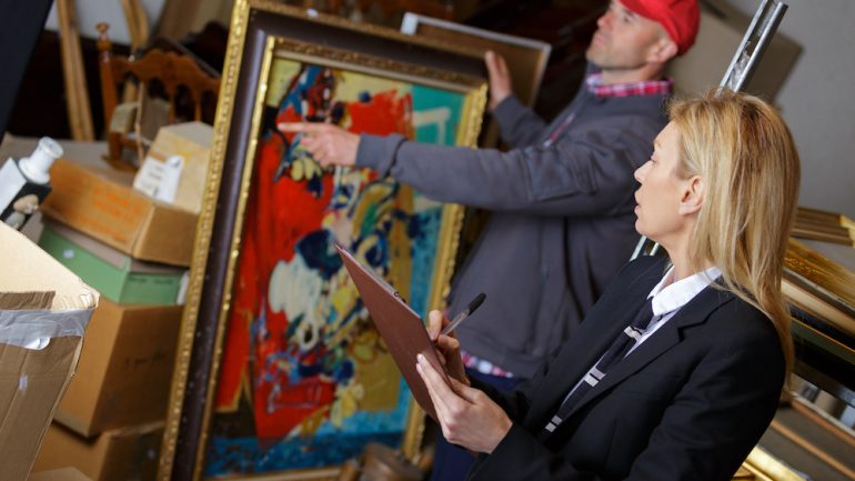 Women working with vendor to sell antiques including a bright colored painting.