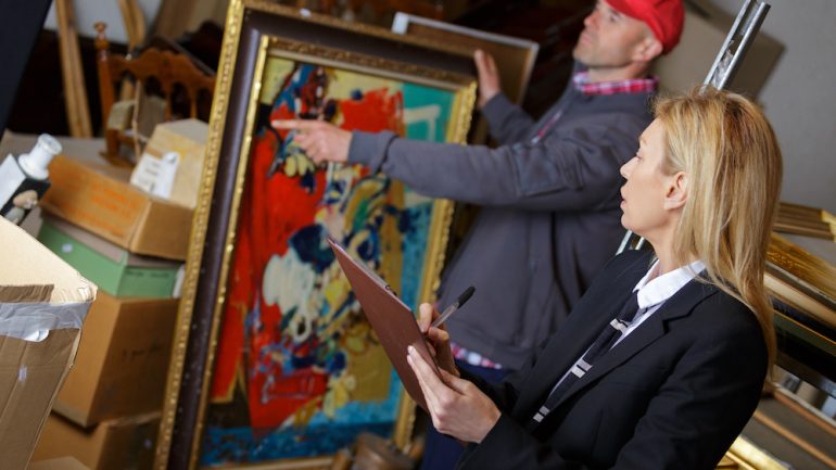 Women working with vendor to sell antiques including a bright colored painting.