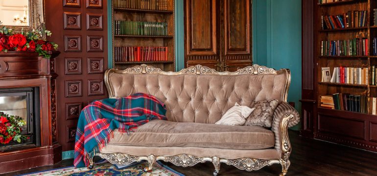 Luxury interior of home library in grandmillennial style. Sitting room with bookshelf, books, arm chair, sofa and fireplace. Clean and modern decoration with vintage furniture.