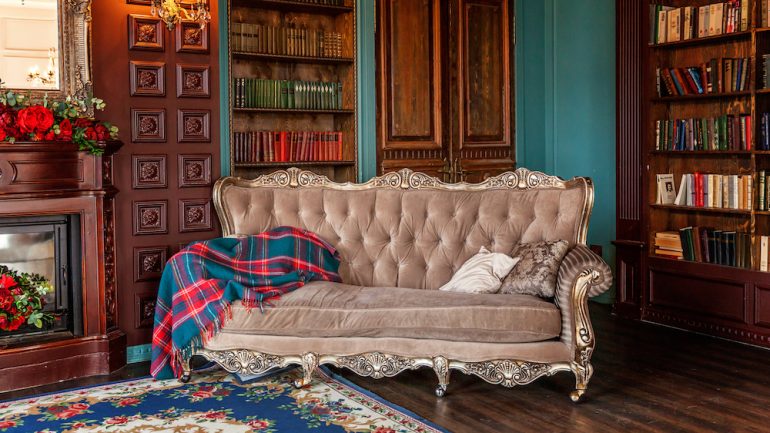 Luxury interior of home library in grandmillennial style. Sitting room with bookshelf, books, arm chair, sofa and fireplace. Clean and modern decoration with vintage furniture.