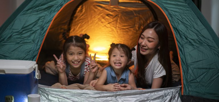 Woman playing and staying in tent with her daughter and having fun with camping tent in their bedroom a staycation lifestyle a new normal for social distancing in coronavirus outbreak situation.