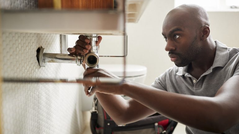 Homeowner conducting plumbing maintenance. Sitting on the floor fixing a bathroom sink pipe.