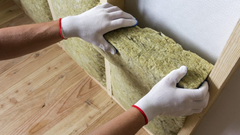 Close-up of worker hands in white gloves insulating rock wool insulation staff in wooden frame for future walls for cold barrier. Comfortable warm home, economy, construction and renovation concept.