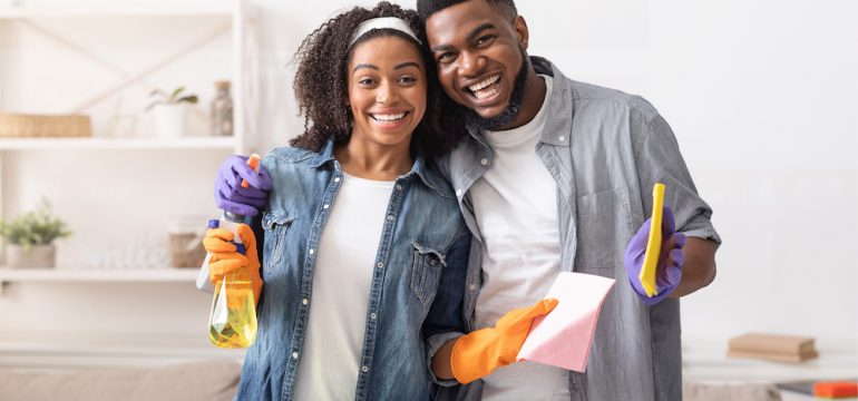 Couple Posing While Cleaning Apartment Together. Holding Detergent Sprayers And Rags while completing tasks on their March To-Dos list.