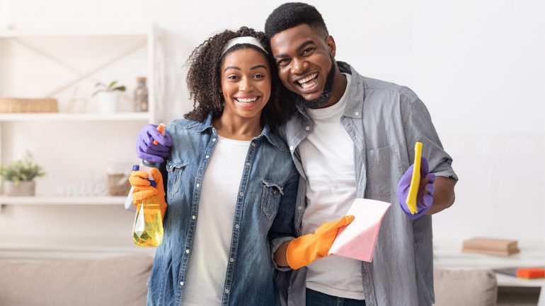 Couple Posing While Cleaning Apartment Together. Holding Detergent Sprayers And Rags while completing tasks on their March To-Dos list.