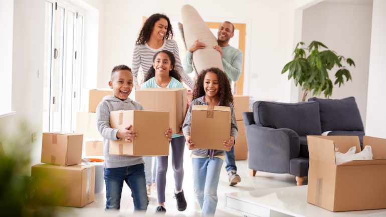 A smiling family of five renting a home, carrying boxes in on moving day.