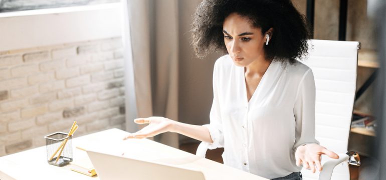 A puzzled woman looks at laptop screen and spreads her hands in disbelief needing a Wi-Fi extender to provide internet coverage.