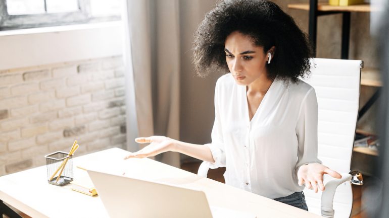 A puzzled woman looks at laptop screen and spreads her hands in disbelief needing a Wi-Fi extender to provide internet coverage.