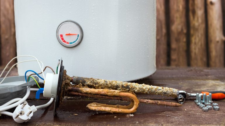 A broken water heater with heating elements, on wooden background.