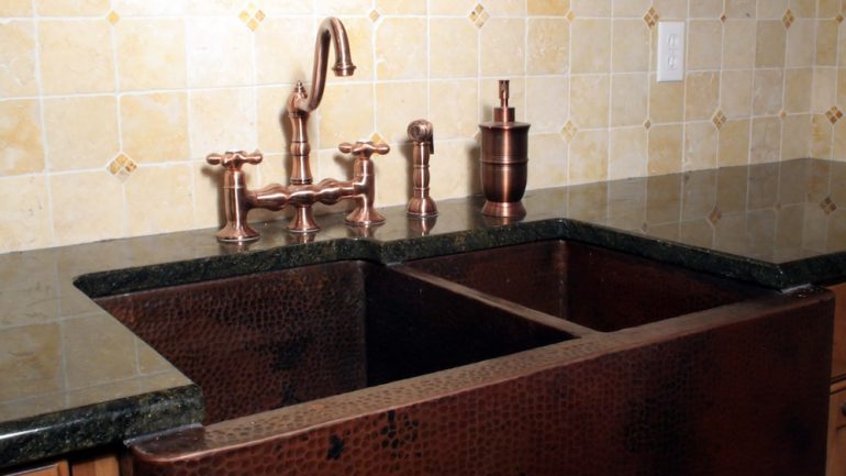 Kitchen sink made of copper materials set in a wood cabinet.