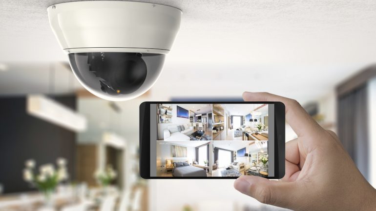 A hand holding a cellular phone connected to a home security camera.