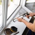 Homeowner performing home maintenance task of sealing window with caulk.