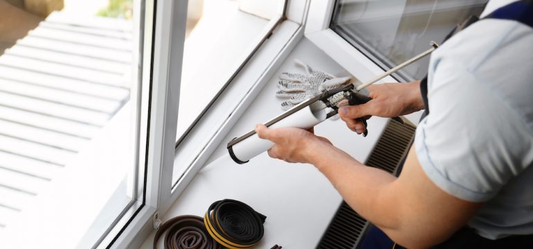 Homeowner performing home maintenance task of sealing window with caulk.