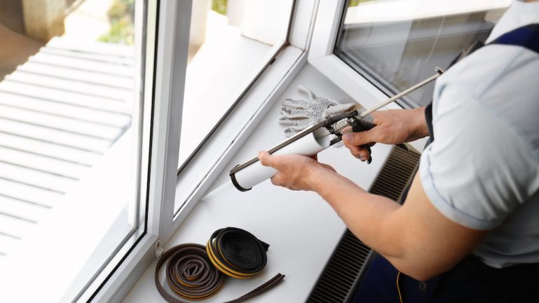Homeowner performing home maintenance task of sealing window with caulk.