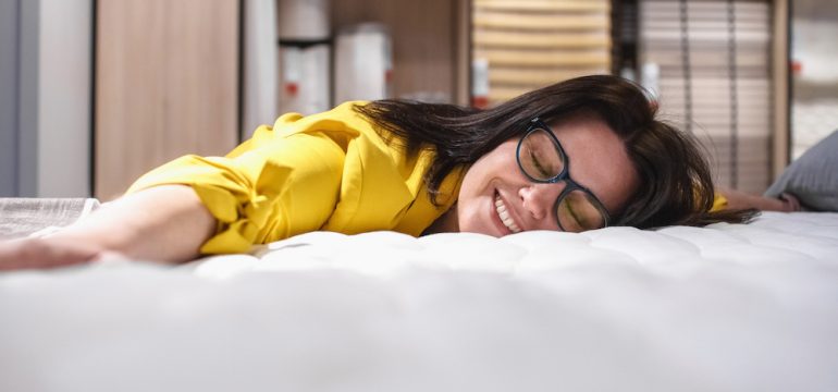 Buying a mattress to replace common household items. A brunette woman laying on a new mattress.