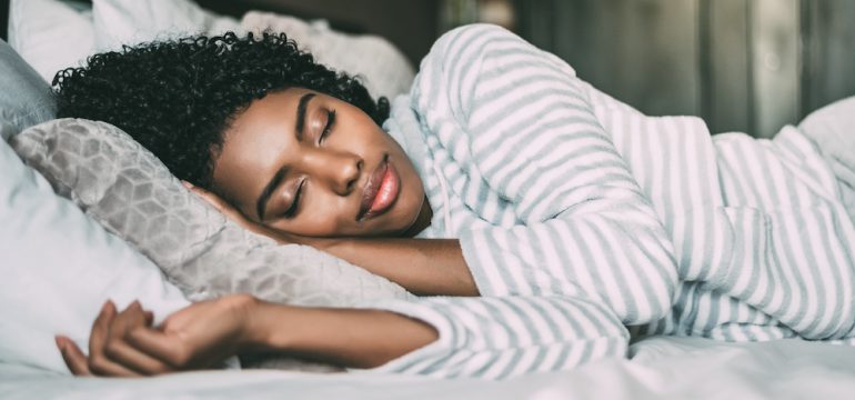 Close up of a pretty woman with curly hair with her eyes closed getting a great night's sleep.