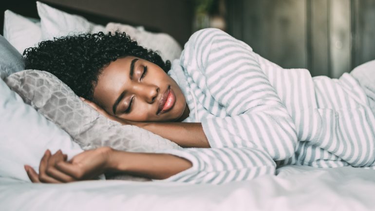 Close up of a pretty woman with curly hair with her eyes closed getting a great night's sleep.