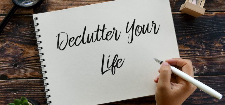 Top view of magnifying glass,sand clock, plant, pen with handwriting "Declutter Your Life" on notebook on wooden background. Theme of how to conquer clutter in your life.