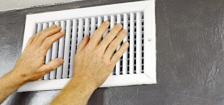A pair of adult male hands feeling the flow of air coming out of an air vent on a wall near a ceiling before shutting vent to save on energy.