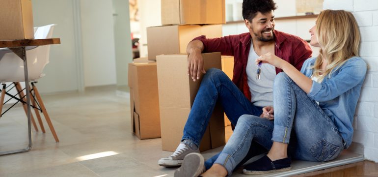 Young married couple moving in new home and unpacking cardboard boxes. They were able to purchase their new home with homeownership incentives for first time buyers.