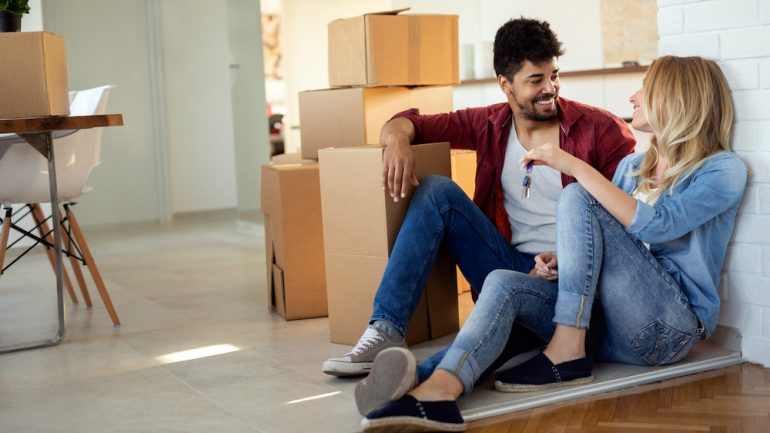 Young married couple moving in new home and unpacking cardboard boxes. They were able to purchase their new home with homeownership incentives for first time buyers.