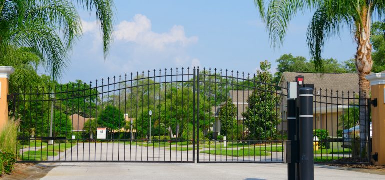 Entrance gate to a beautiful gated private community with lush green trees and grass.