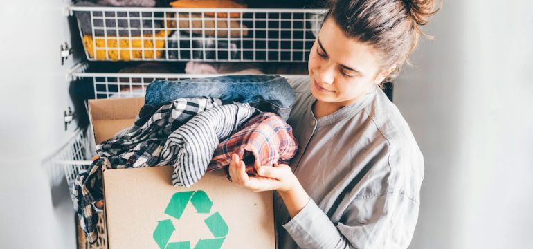 Recycle summer and winter clothes concept. Young woman with recycling box full clothes.