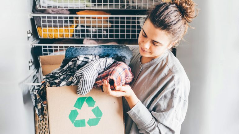 Recycle summer and winter clothes concept. Young woman with recycling box full clothes.