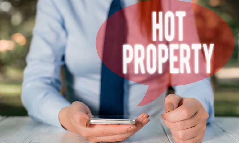 Male holding a calculator trying to figure out how to buy a house before you sell in a seller's market with the words hot property across photo